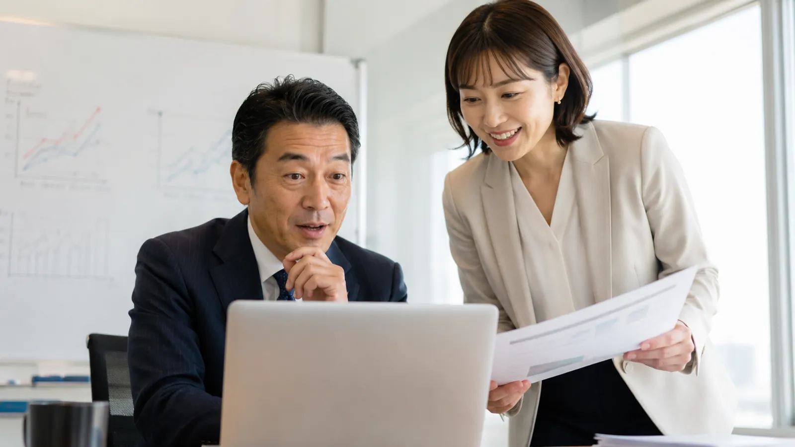会議室で日本人の経営者と社員がノートパソコンの画面を一緒に見て、気づいたような表情をしている場面
